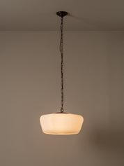 A modern pendant light with a warm white frosted glass shade suspended by a dark metal chain from a ceiling mount, set against a neutral beige wall.