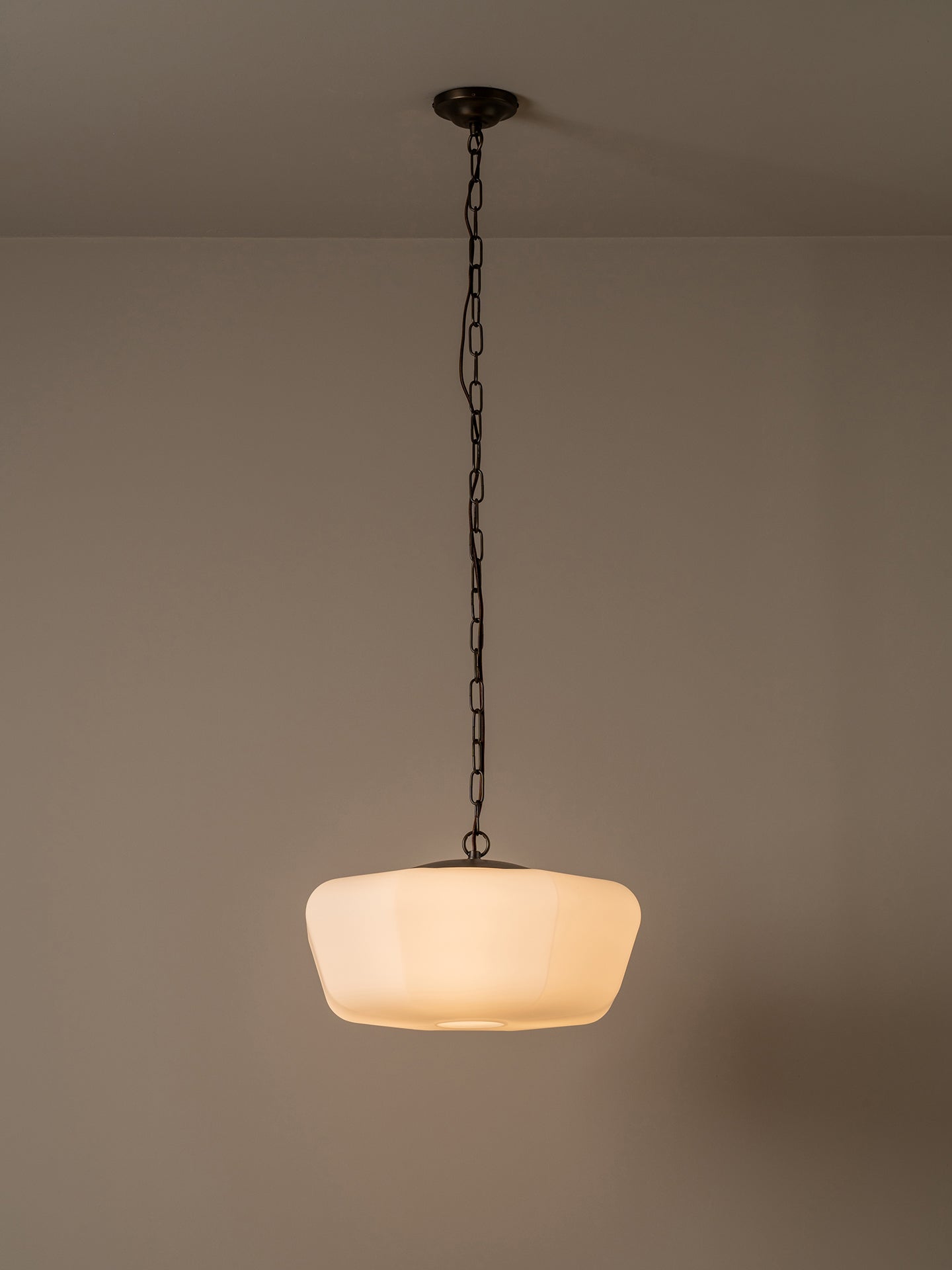 A modern pendant light with a warm white, rounded ribbed glass shade hanging from a dark metal chain and ceiling canopy against a neutral beige wall.