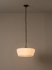 A modern pendant light with a warm white, rounded ribbed glass shade hanging from a dark metal chain and ceiling canopy against a neutral beige wall.