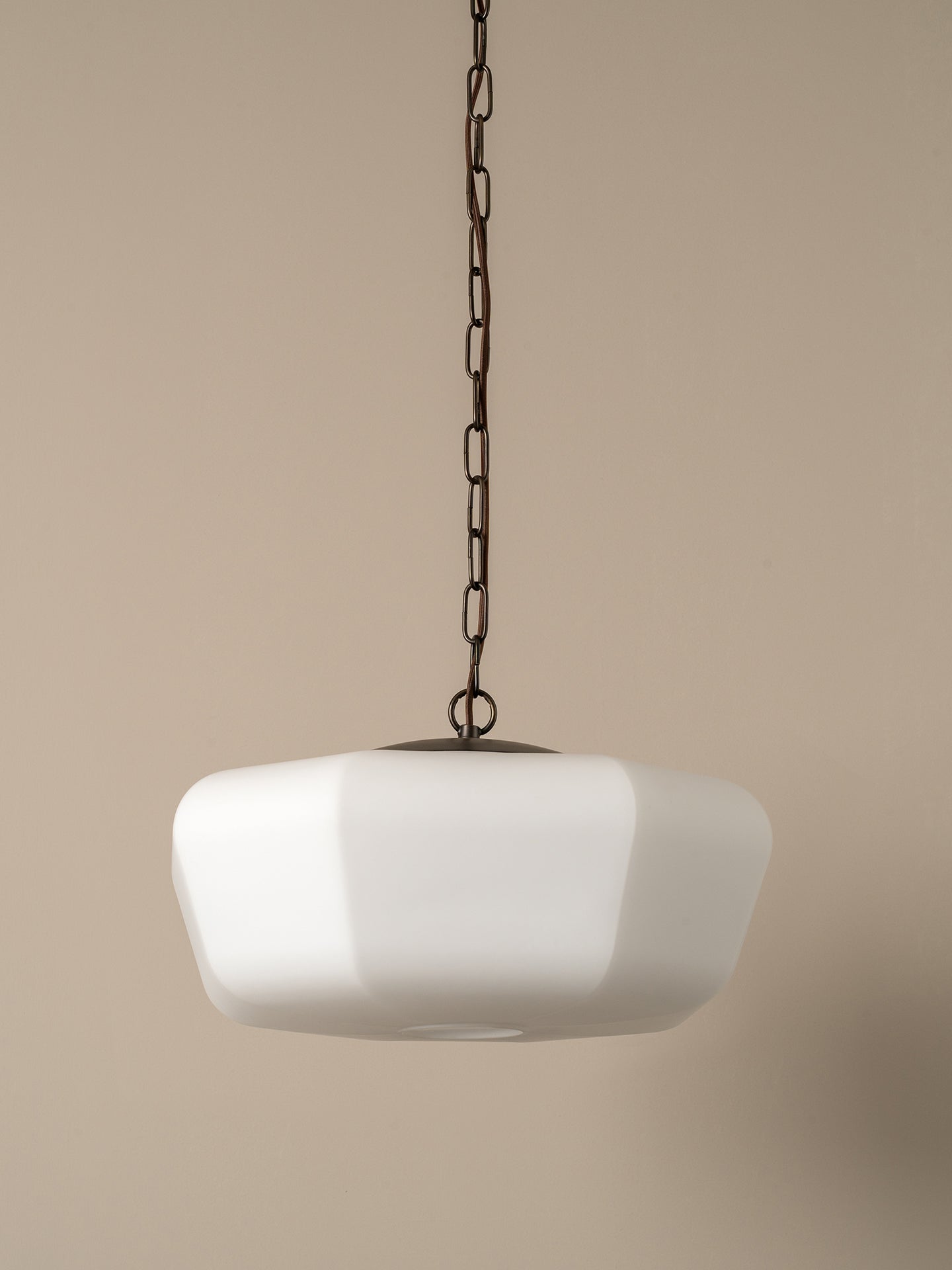 A modern pendant light with a wide, rounded white glass shade suspended from a black metal chain against a solid beige background.