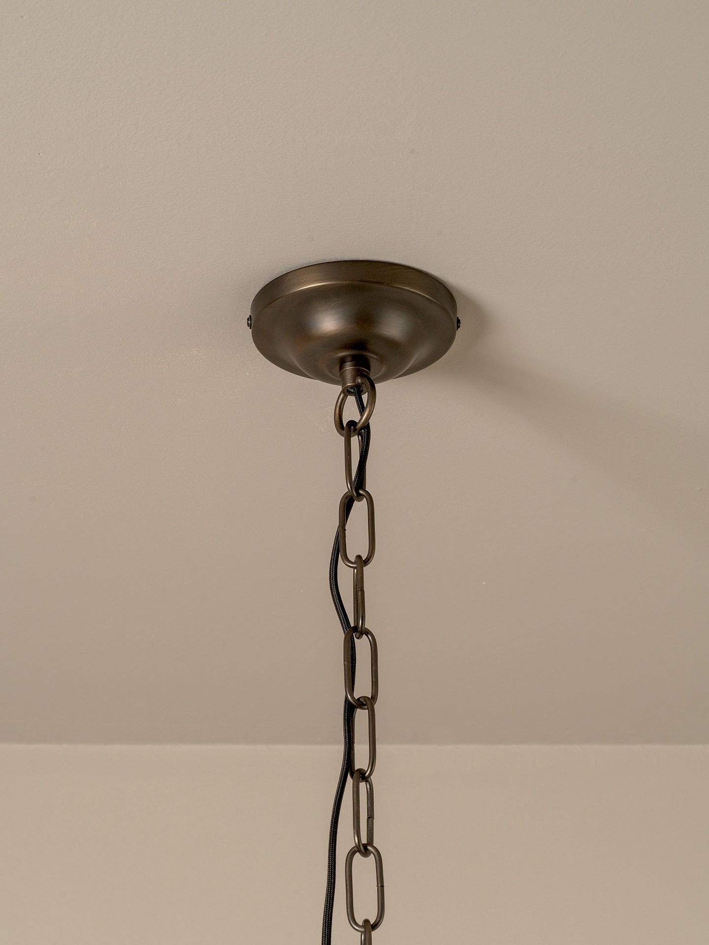 An industrial-style ceiling light fixture with a dark bronze metal ceiling canopy and chain hanging from a beige ceiling.