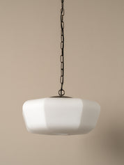 A modern pendant light with a wide, rounded white glass shade suspended from a dark metal chain against a solid beige background.