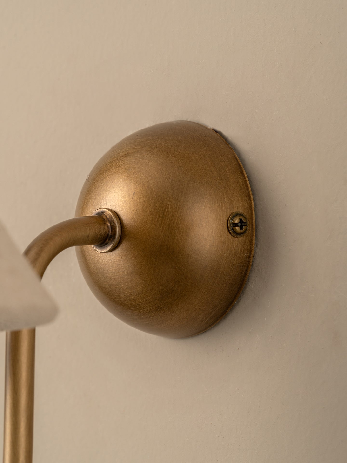  a curved brass arm, mounted on a beige wall.