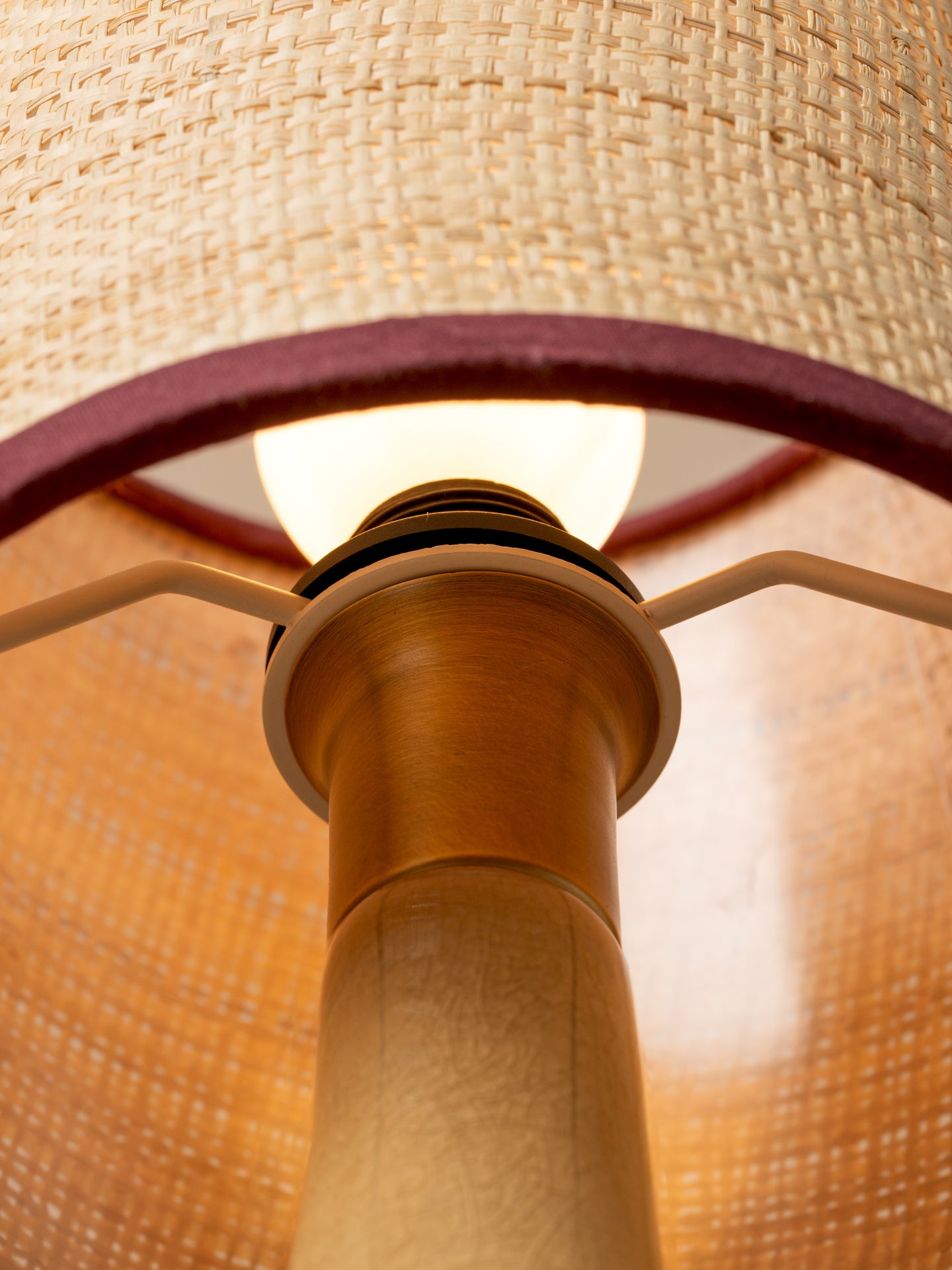 Close-up of a lamp with a woven natural-fiber shade, warm glowing bulb, and light wood column.