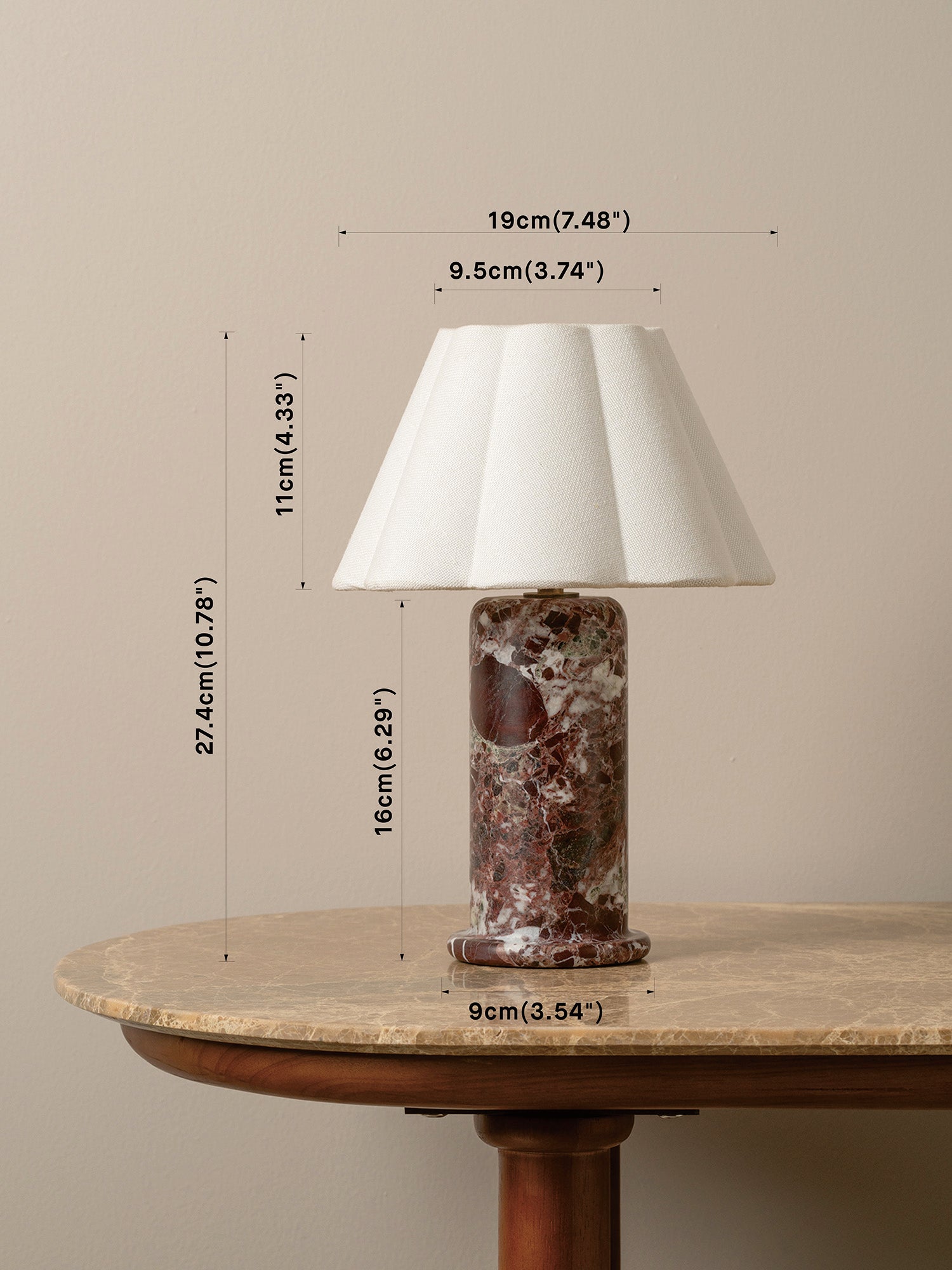 A table lamp with a white pleated drum shade and a reddish-brown marbled base sits on a round wooden table against a beige wall, with overlaid dimension lines and text showing measurements of 19 cm top diameter, 11 cm shade height, 16 cm body height, and 9 cm base diameter.