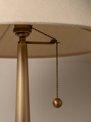Close-up of a brass pull-chain lamp with a beige fabric shade and a matching brass ball pull.