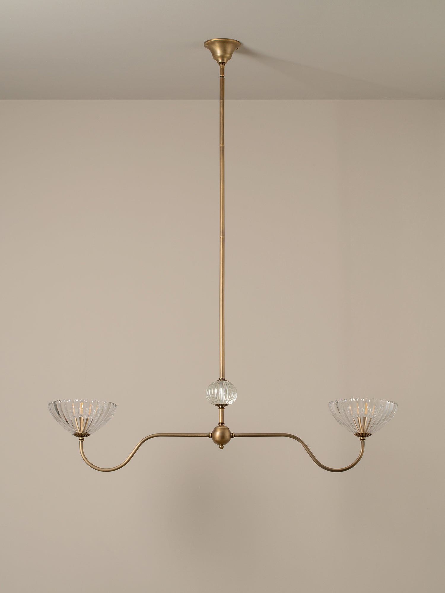 A three-light brass chandelier with clear ribbed glass shades, suspended from a central clear glass orb, shown against a neutral beige wall and ceiling.