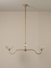 A three-light brass chandelier with clear ribbed glass shades, suspended from a central clear glass orb, shown against a neutral beige wall and ceiling.