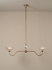 A three-light brass chandelier with a central glass globe and two curved arms ending in fluted clear glass shades, shown hanging against a plain beige wall.