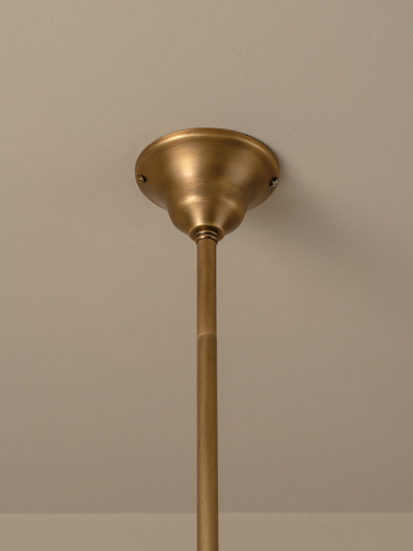 A close-up of a brass ceiling light fixture showing the ceiling canopy and downrod against a neutral beige wall.