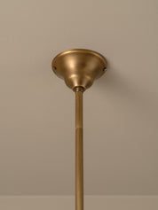 A close-up of a brass ceiling light fixture showing the ceiling canopy and downrod against a neutral beige wall.