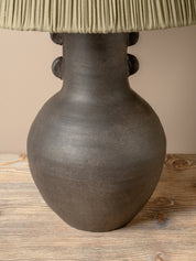 A table lamp with a dark brown ceramic vase-shaped base and a pleated olive green fabric shade