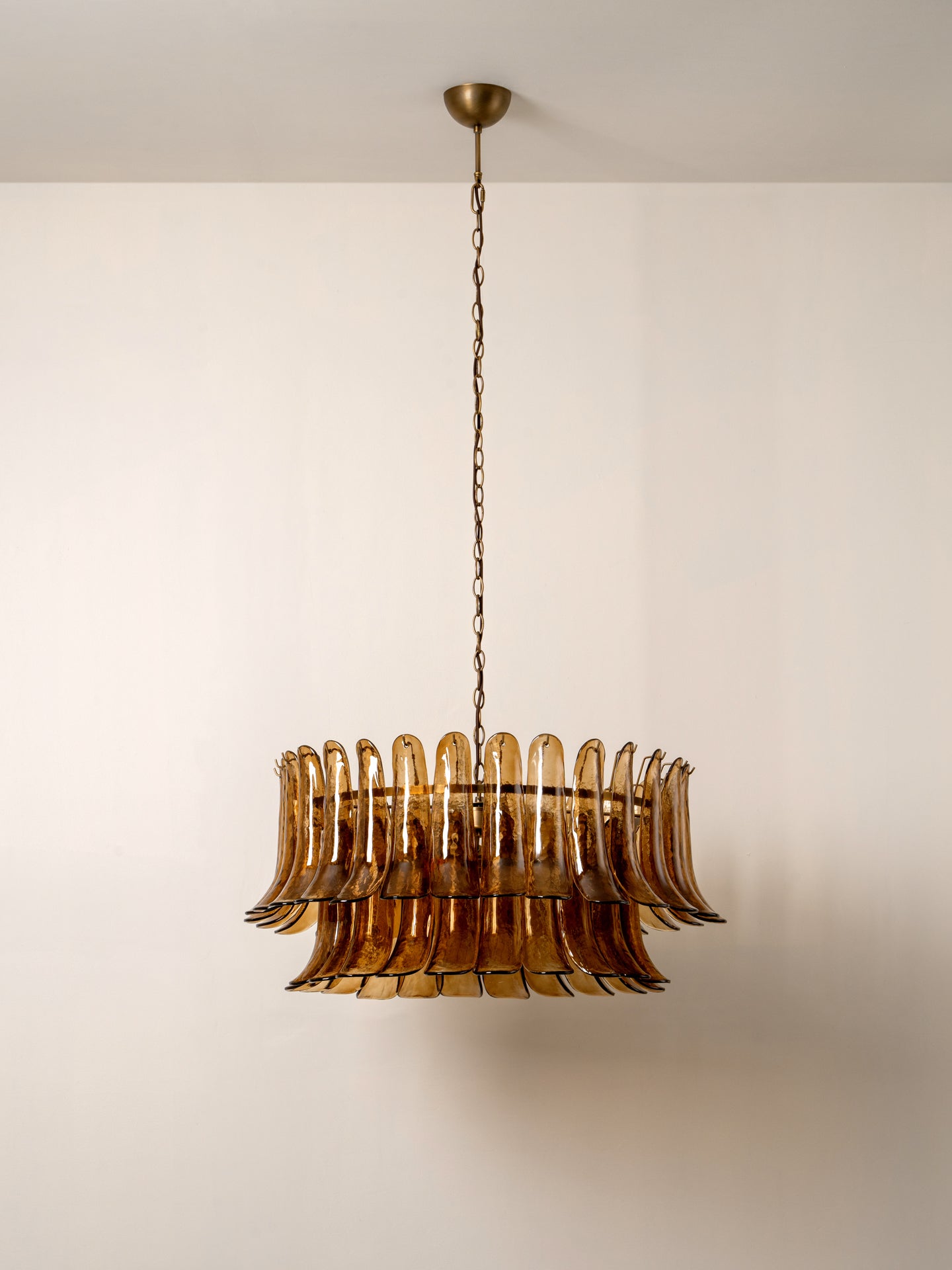 A vintage-style amber glass chandelier with a fluted, layered circular design, suspended by a brass chain from a matching ceiling canopy against a plain off-white wall.