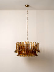 A vintage-style amber glass chandelier with a fluted, layered circular design, suspended by a brass chain from a matching ceiling canopy against a plain off-white wall.