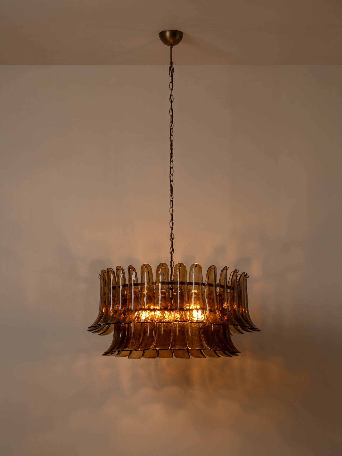 A vintage-style amber glass chandelier with a tiered, fluted design, suspended by a dark chain from a ceiling in a warm, dimly lit room.