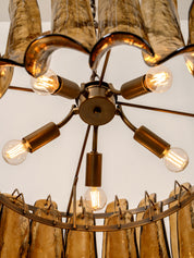 A close-up of a multi-light chandelier with warm amber glass shades and brass-finished metal arms, with several clear bulb sockets illuminated against a plain light background.