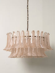 A mid-century modern tiered chandelier featuring translucent blush pink glass fluted tubes suspended from a dark metal frame and chain.