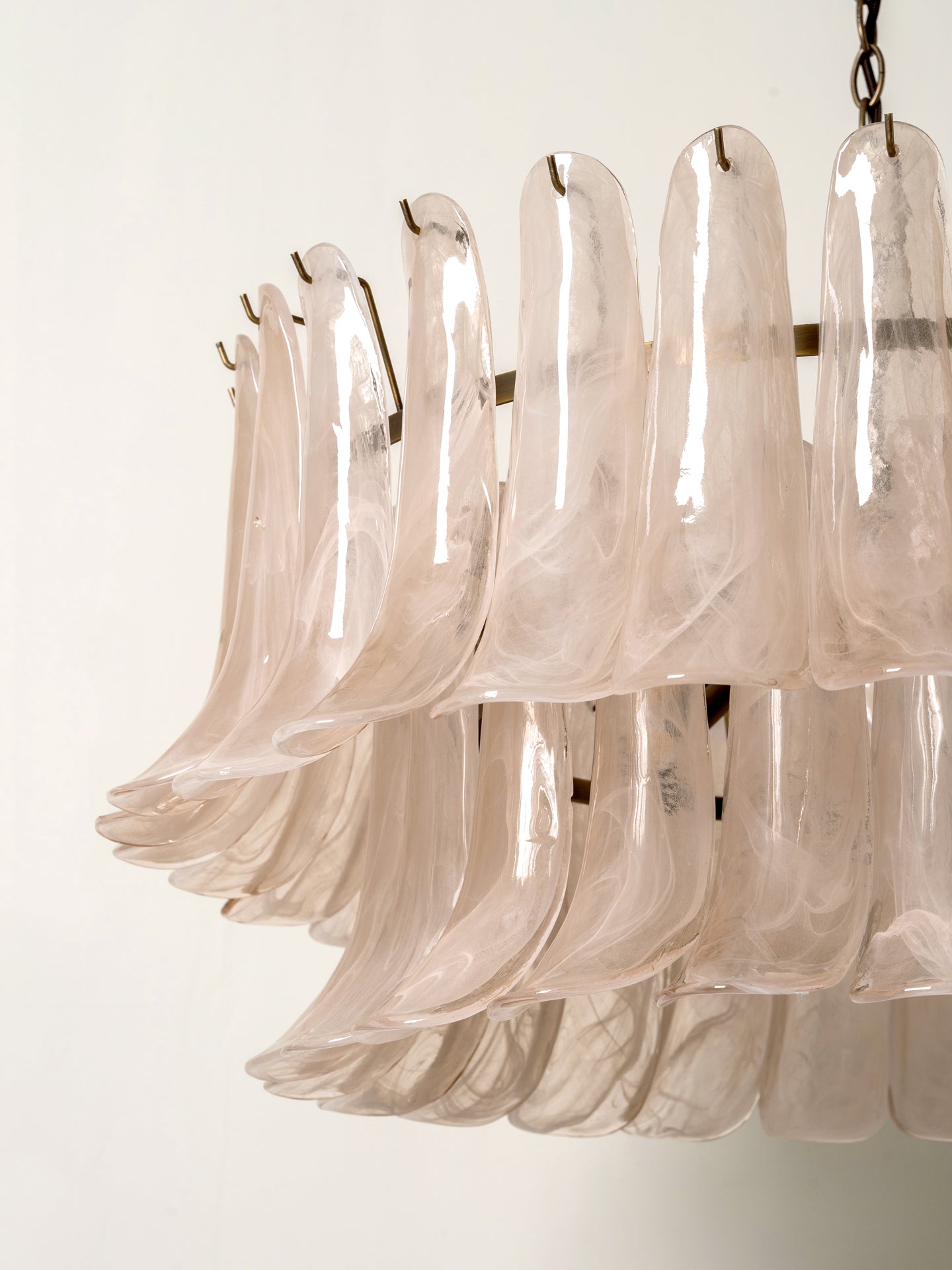 A close-up of a modern chandelier featuring multiple layers of translucent, bell-shaped glass shades in a pale blush pink color, suspended from a dark metal ring.