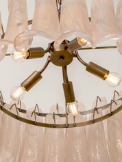 A close-up of a modern chandelier featuring a brass-finished central hub with six arms extending to clear glass bell-shaped shades and hanging glass rods.