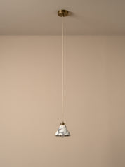 A modern pendant light with a white and gray marble cone shade, suspended by a thin cord from a brass ceiling canopy against a warm beige wall.