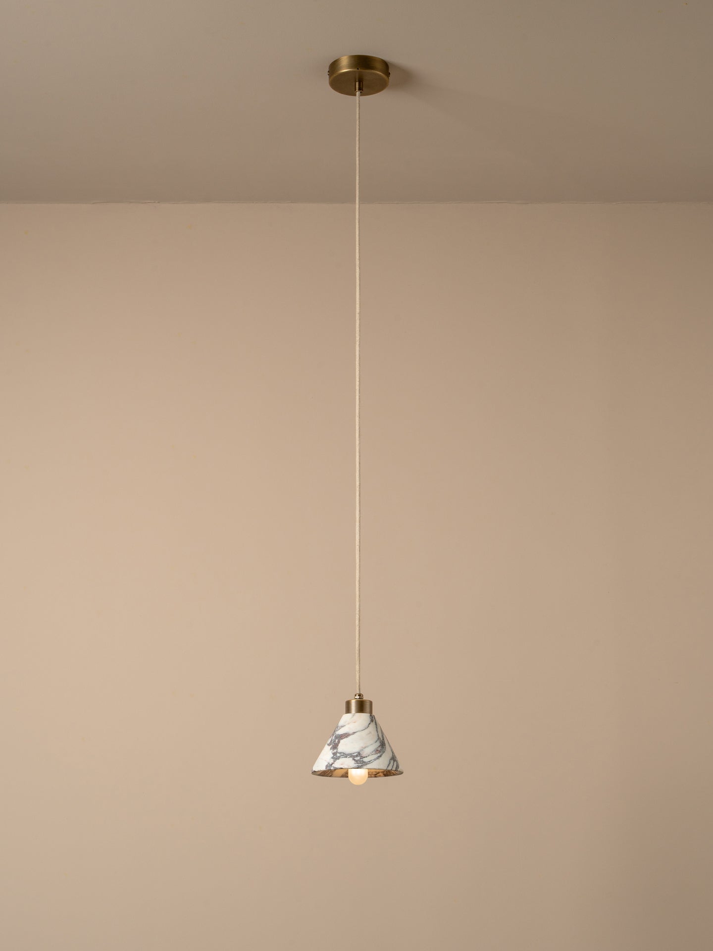 A modern pendant light with a white and gray marble cone shade, a gold-toned metal rim, and a slim white cord hanging from a gold ceiling canopy against a warm beige wall.