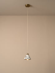 A modern pendant light with a white and gray marble cone shade, a gold-toned metal rim, and a slim white cord hanging from a gold ceiling canopy against a warm beige wall.