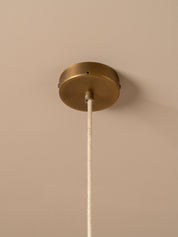 A close-up of a ceiling light fixture showing a round brass canopy mounted on a beige wall or ceiling, with a white fabric cord hanging down.