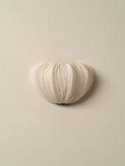 A small, organic-shaped wall sconce with a textured, pleated fabric or paper-like surface in a warm off-white/cream color, mounted on a solid beige wall.