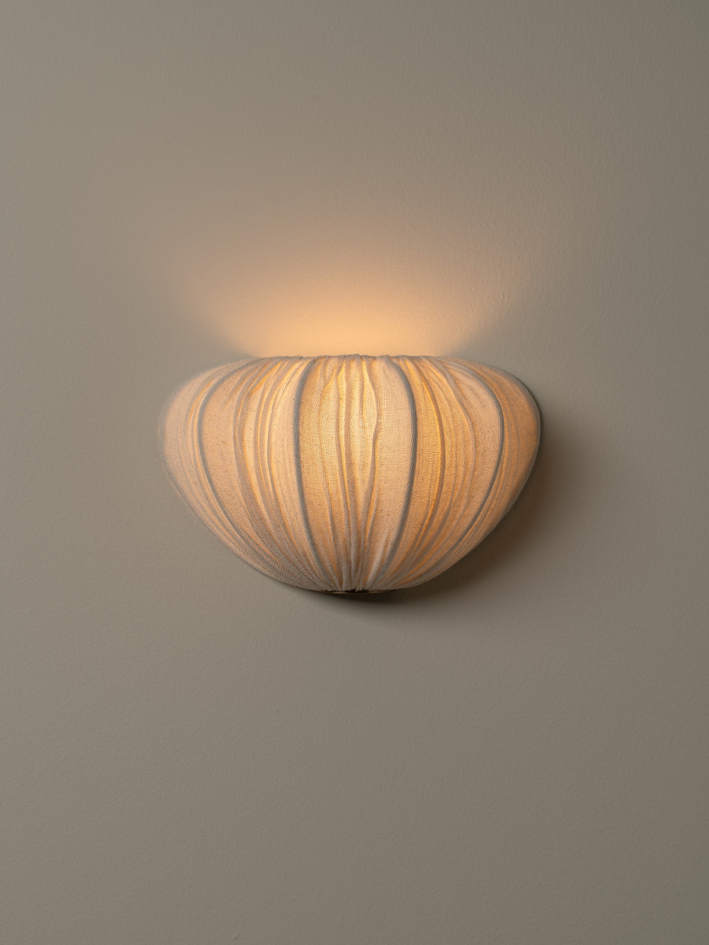 A modern wall sconce with a ribbed, organic shell-like shade, illuminated with a warm yellow glow against a neutral gray wall.