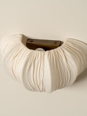 A close-up of a cream-colored fabric-covered wall hook with a textured, gathered design and a dark metal mounting bracket.