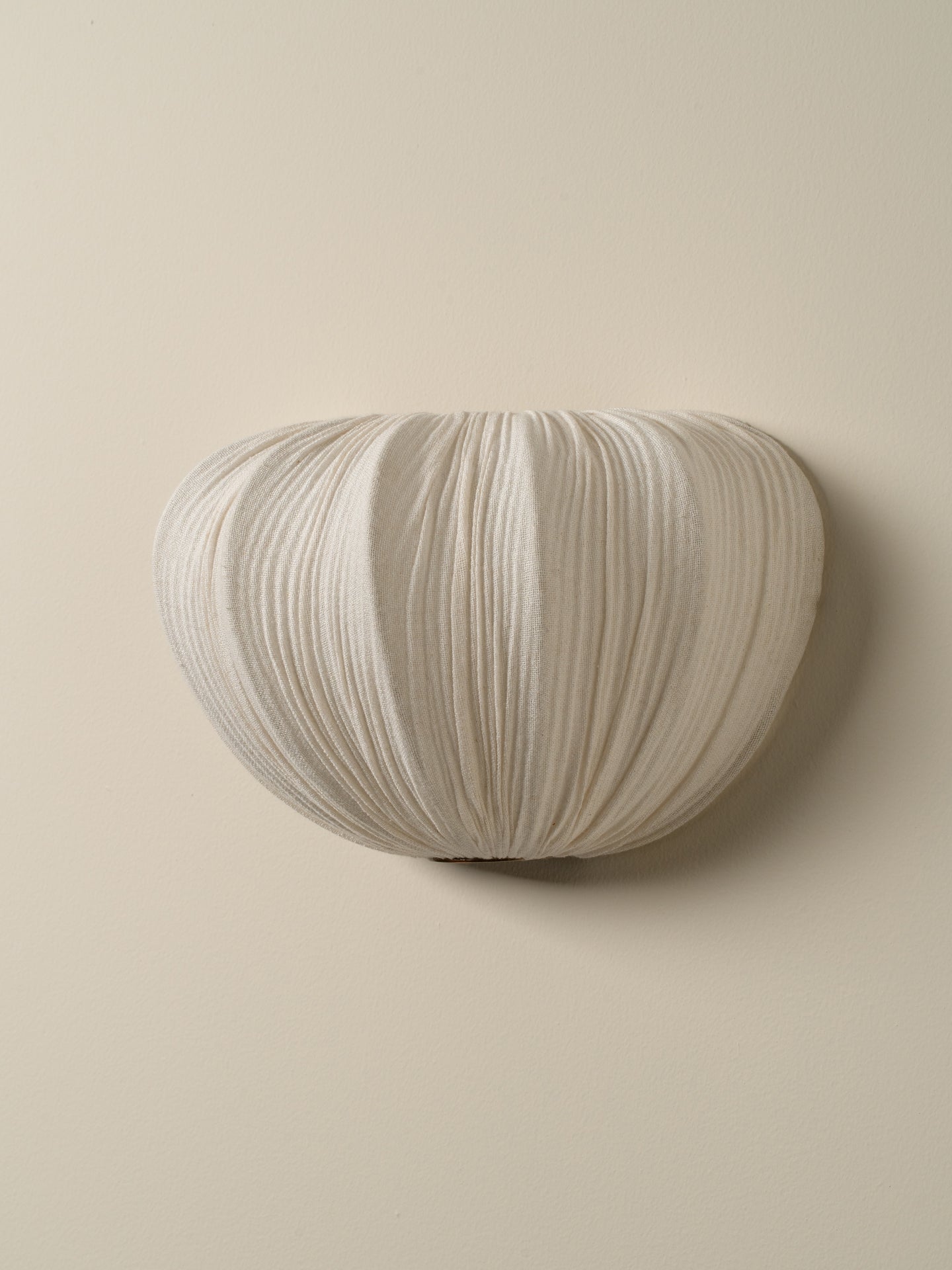 An off-white pleated fabric wall sconce mounted on a solid beige wall.