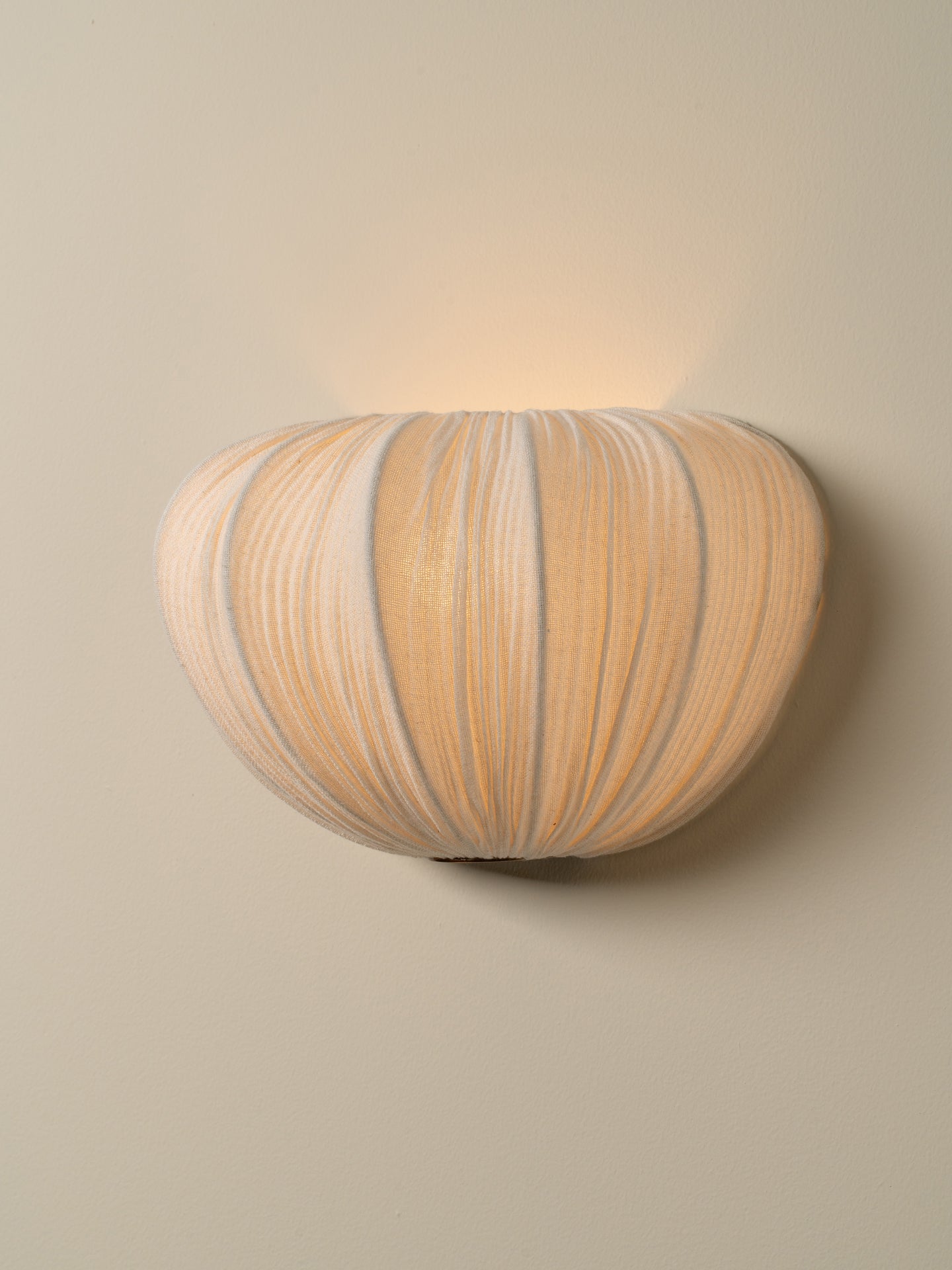 A modern wall sconce light fixture with a ribbed, pumpkin-like organic shape, mounted on a warm beige wall and casting a soft glow upward.