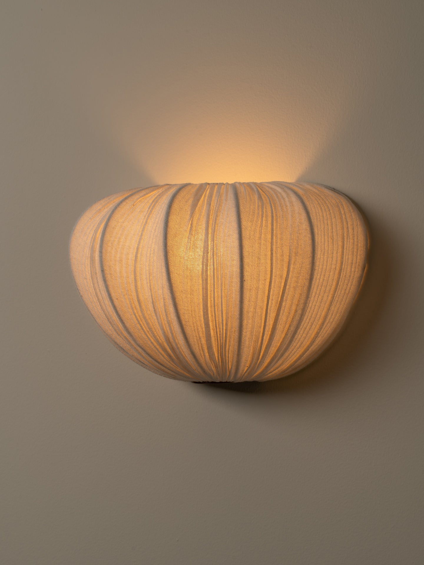 A warm, ribbed wall sconce light fixture with a rounded, pumpkin-like shape, mounted on a neutral gray wall and casting a soft glow upward.