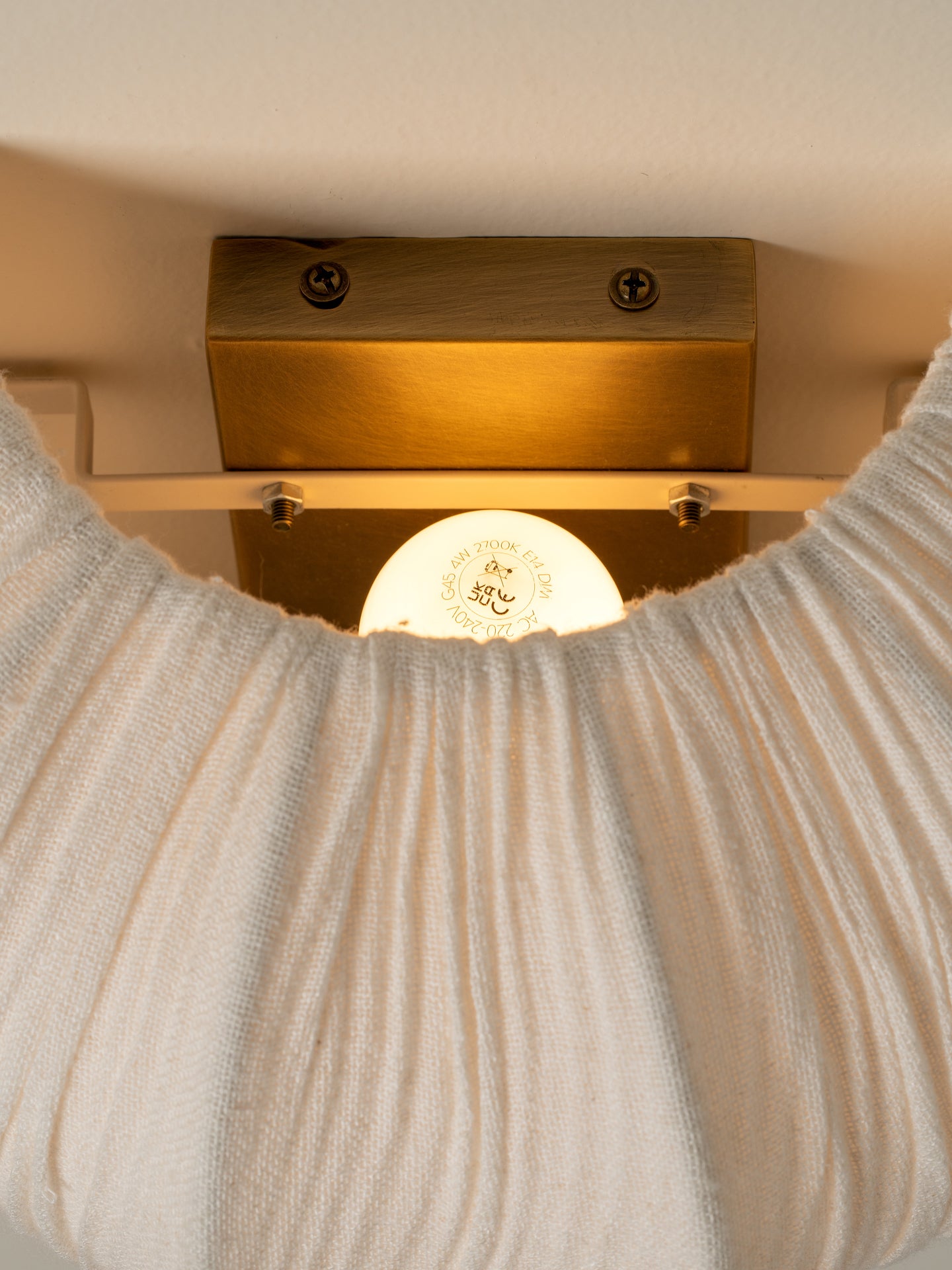 A close-up of a ribbed cream knit garment, likely a sweater or scarf, draped in front of a warm brass wall light fixture.