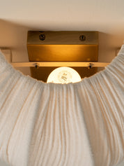 A close-up of a ribbed cream knit garment, likely a sweater or scarf, draped in front of a warm brass wall light fixture.