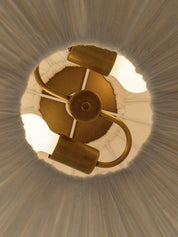 An overhead close-up of a brass ceiling light fixture with three arms and glowing bulbs, set against a white pleated lampshade.