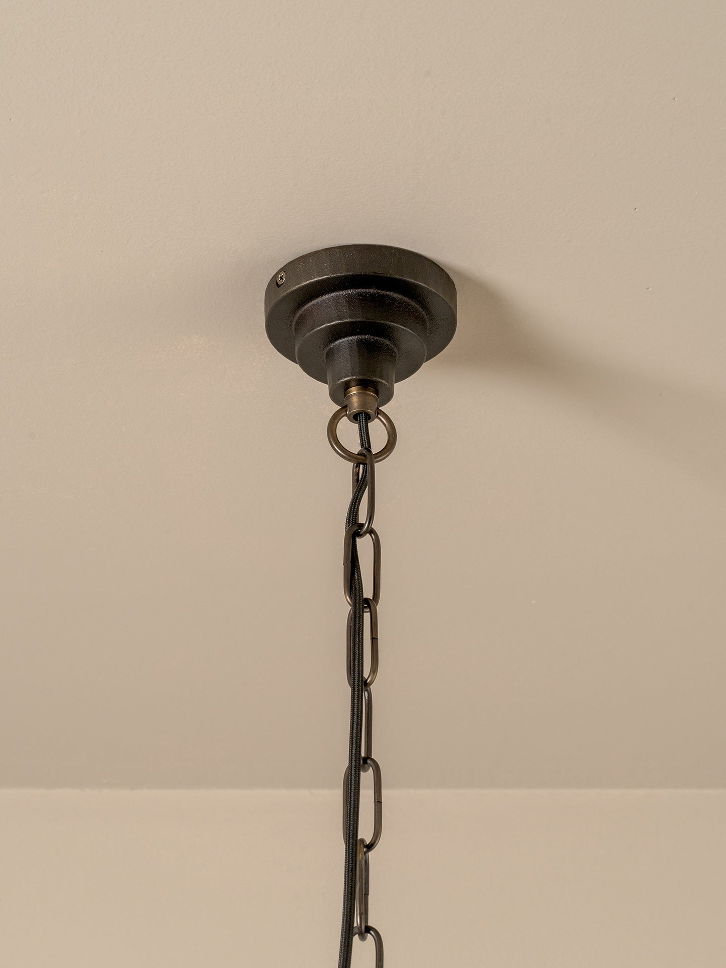 A close-up of a dark metal ceiling canopy and hanging chain fixture against a plain off-white wall.