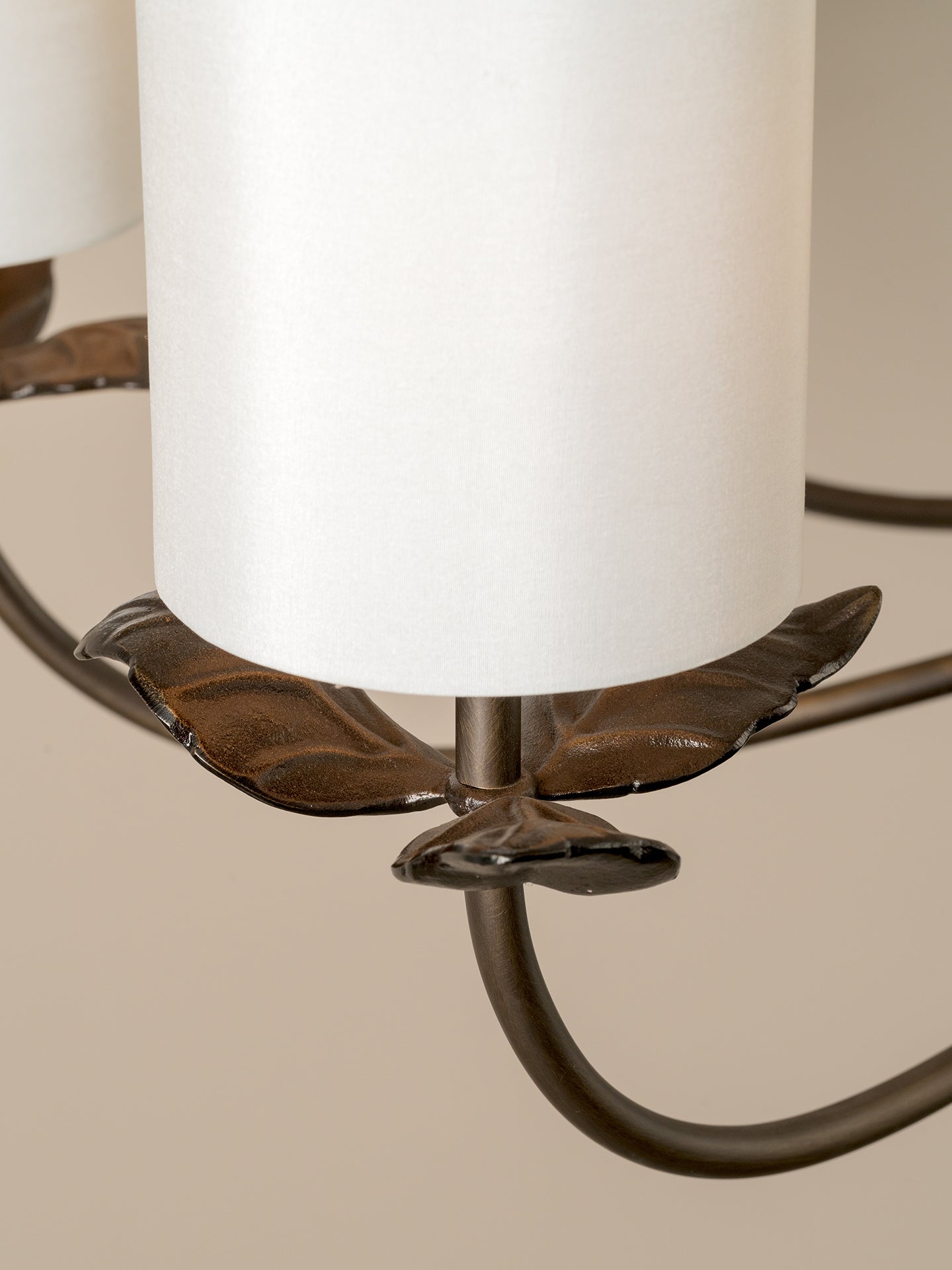 Close-up of a chandelier light fixture with a white cylindrical shade and a dark bronze metal frame featuring leaf-like accents.