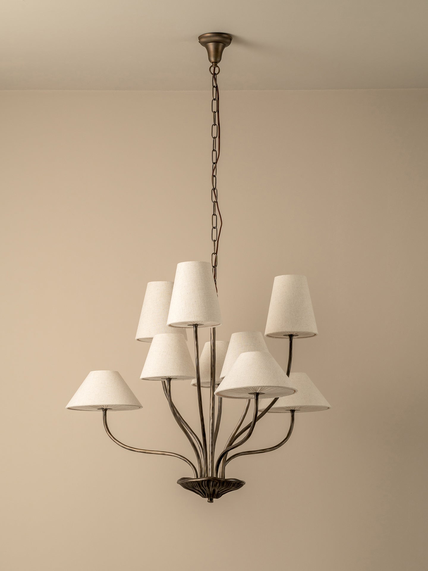 A multi-light chandelier with a dark metal frame and white fabric drum shades, hanging from a chain against a plain beige wall.