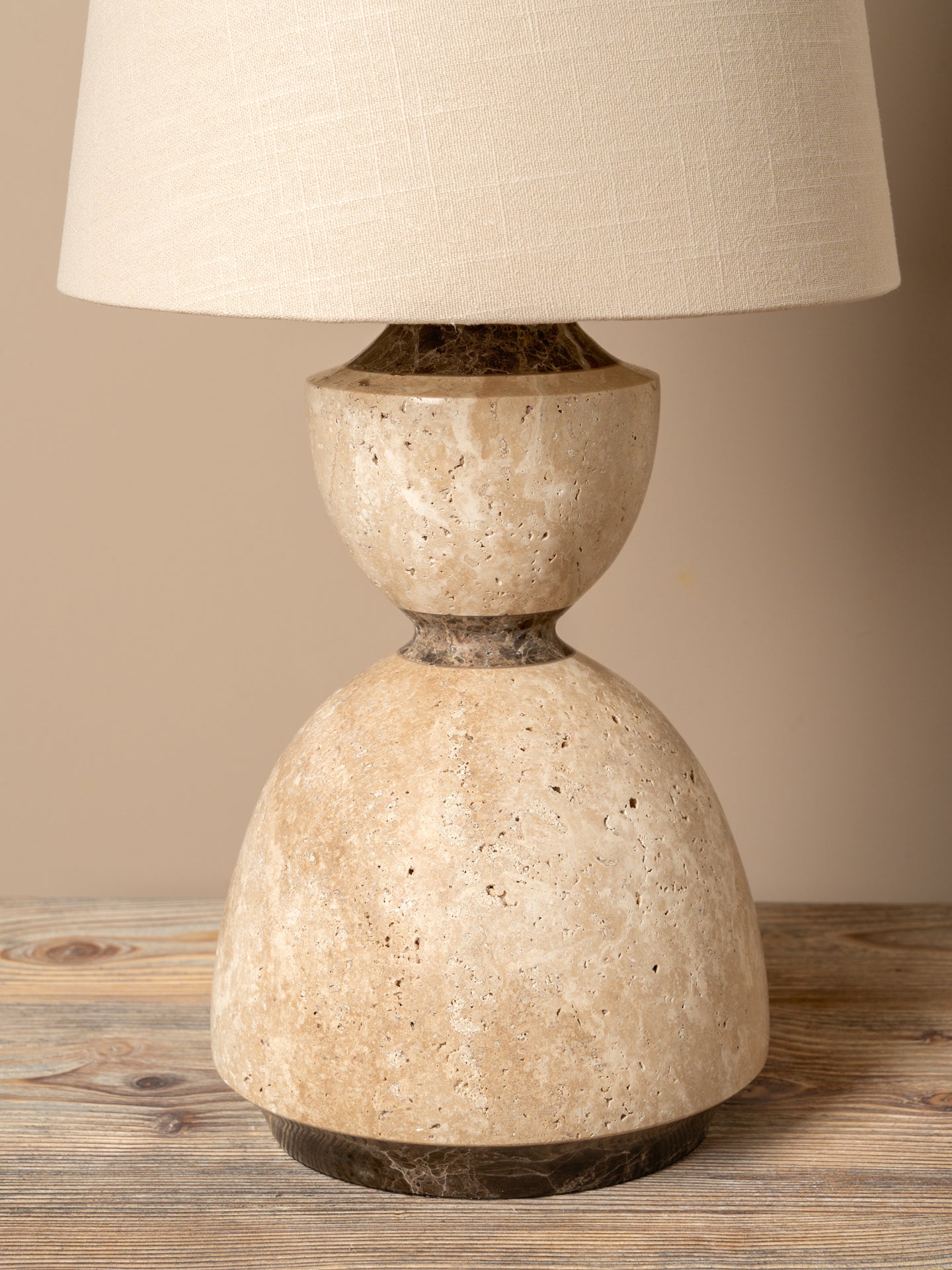A table lamp with a textured beige stone base and a matching fabric drum shade, set on a rustic wooden surface against a neutral beige background.