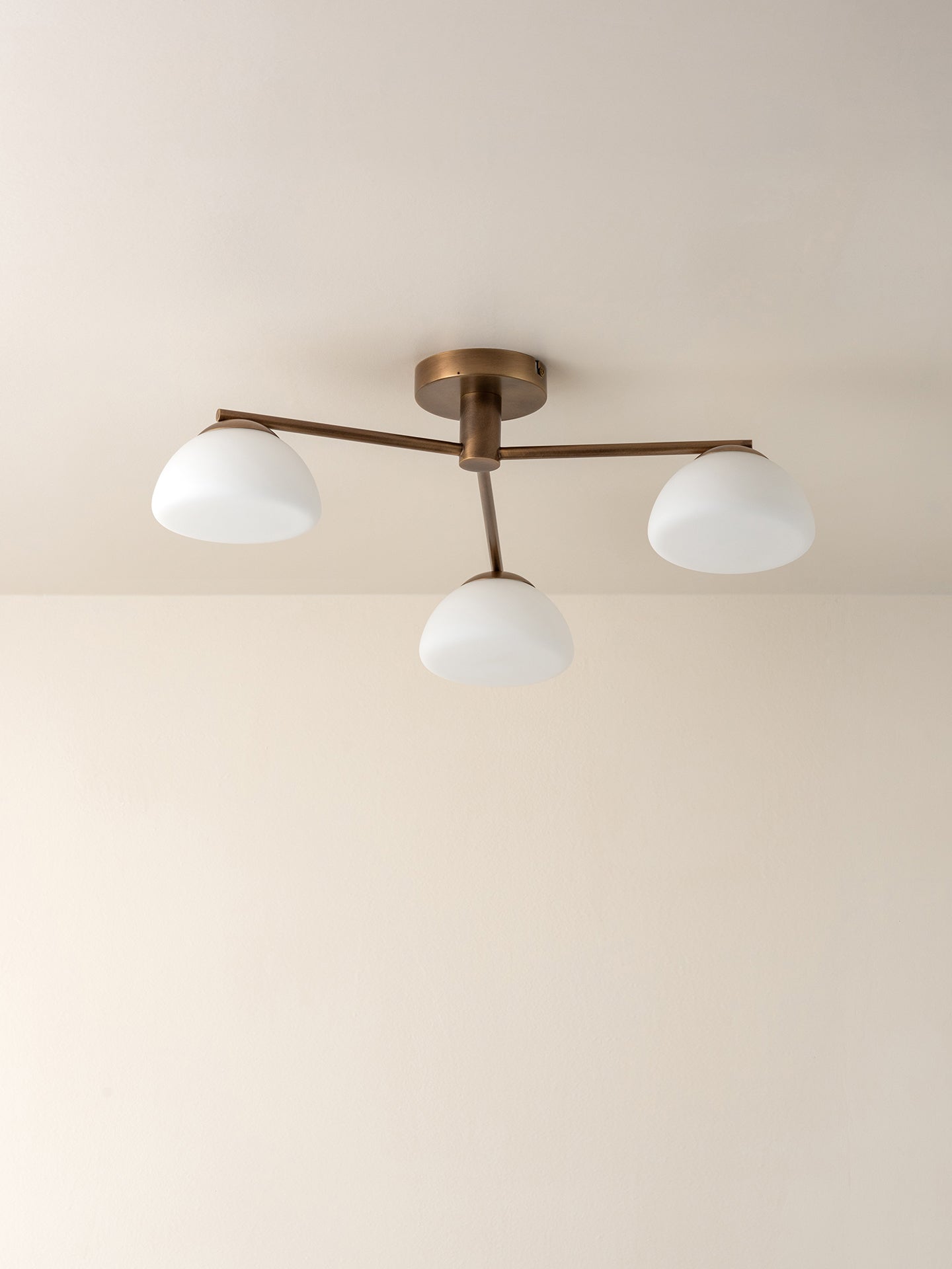 A three-light semi-flush mount ceiling fixture with a bronze-finished metal frame and three white dome-shaped glass shades, shown installed on a plain beige ceiling.