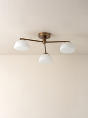 A three-light semi-flush mount ceiling fixture with a bronze-finished metal frame and three white dome-shaped glass shades, shown installed on a plain beige ceiling.