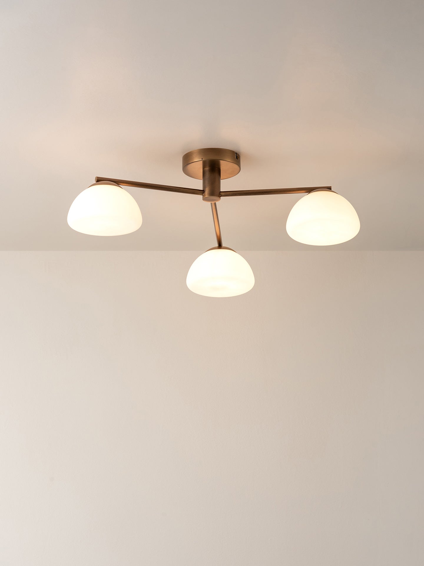 A modern three-light ceiling fixture with a warm brass finish and frosted white glass shades, shown installed on a plain white ceiling.