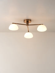 A modern three-light ceiling fixture with a warm brass finish and frosted white glass shades, shown installed on a plain white ceiling.