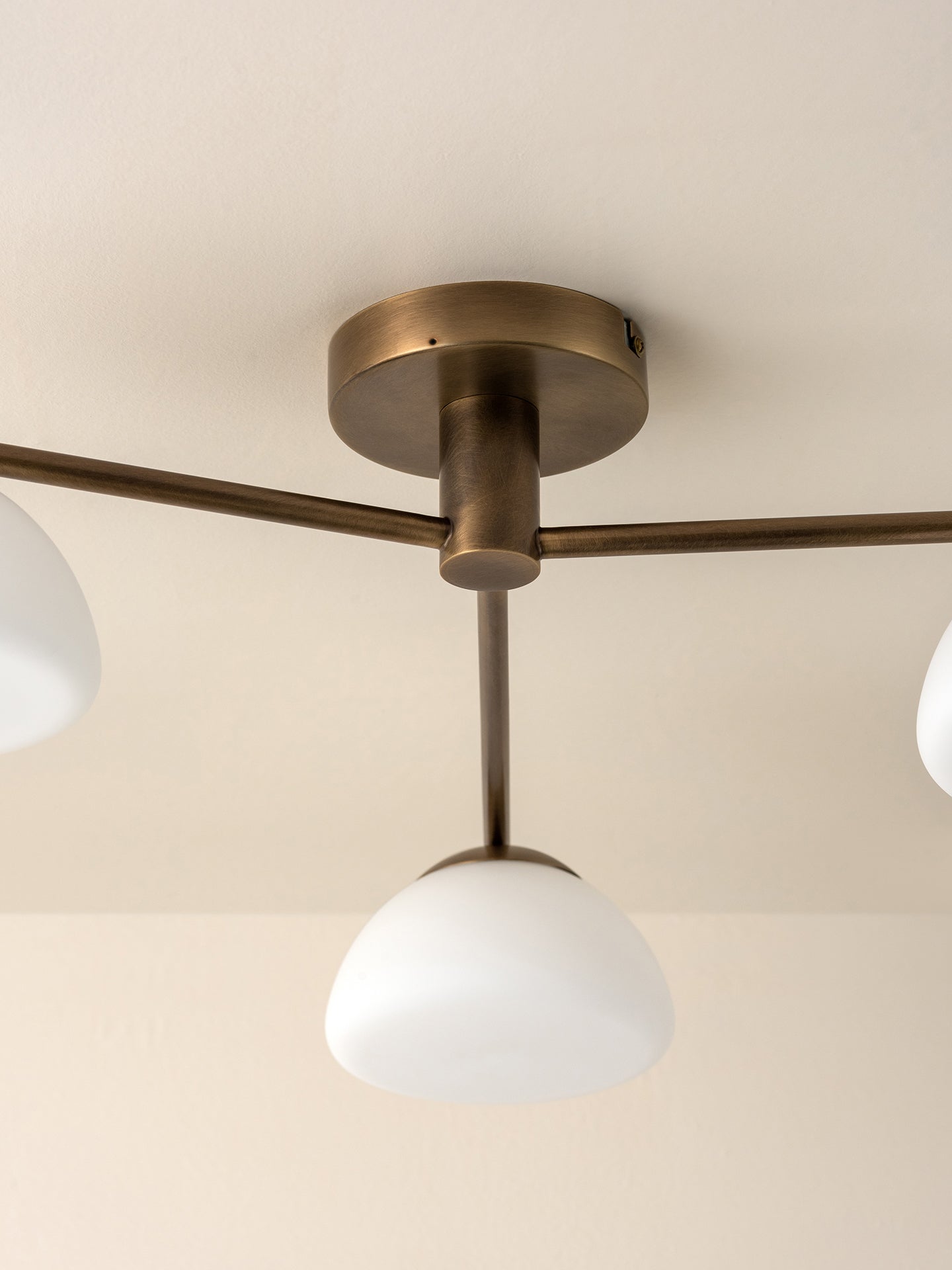 A close-up of a ceiling-mounted light fixture with a round brass-toned ceiling canopy, horizontal arms, and three white dome-shaped glass shades.