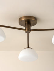 A close-up of a ceiling-mounted light fixture with a round brass-toned ceiling canopy, horizontal arms, and three white dome-shaped glass shades.