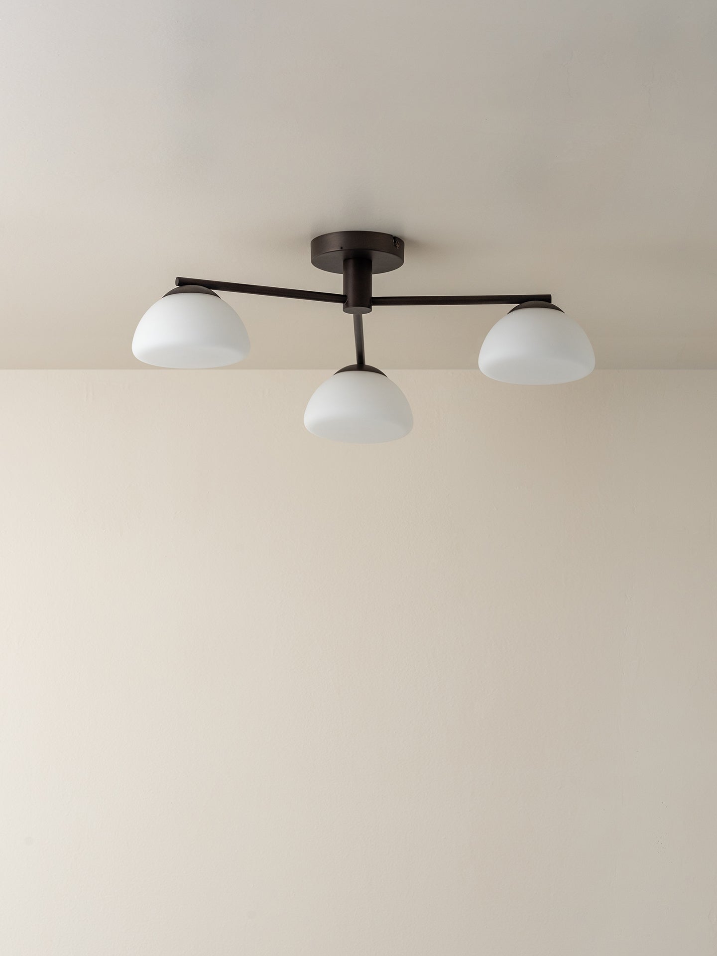 A modern three-light ceiling fixture with a dark metal frame and three white dome-shaped glass shades, mounted on a plain beige ceiling.