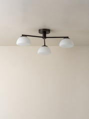 A modern three-light ceiling fixture with a dark metal frame and three white dome-shaped glass shades, mounted on a plain beige ceiling.