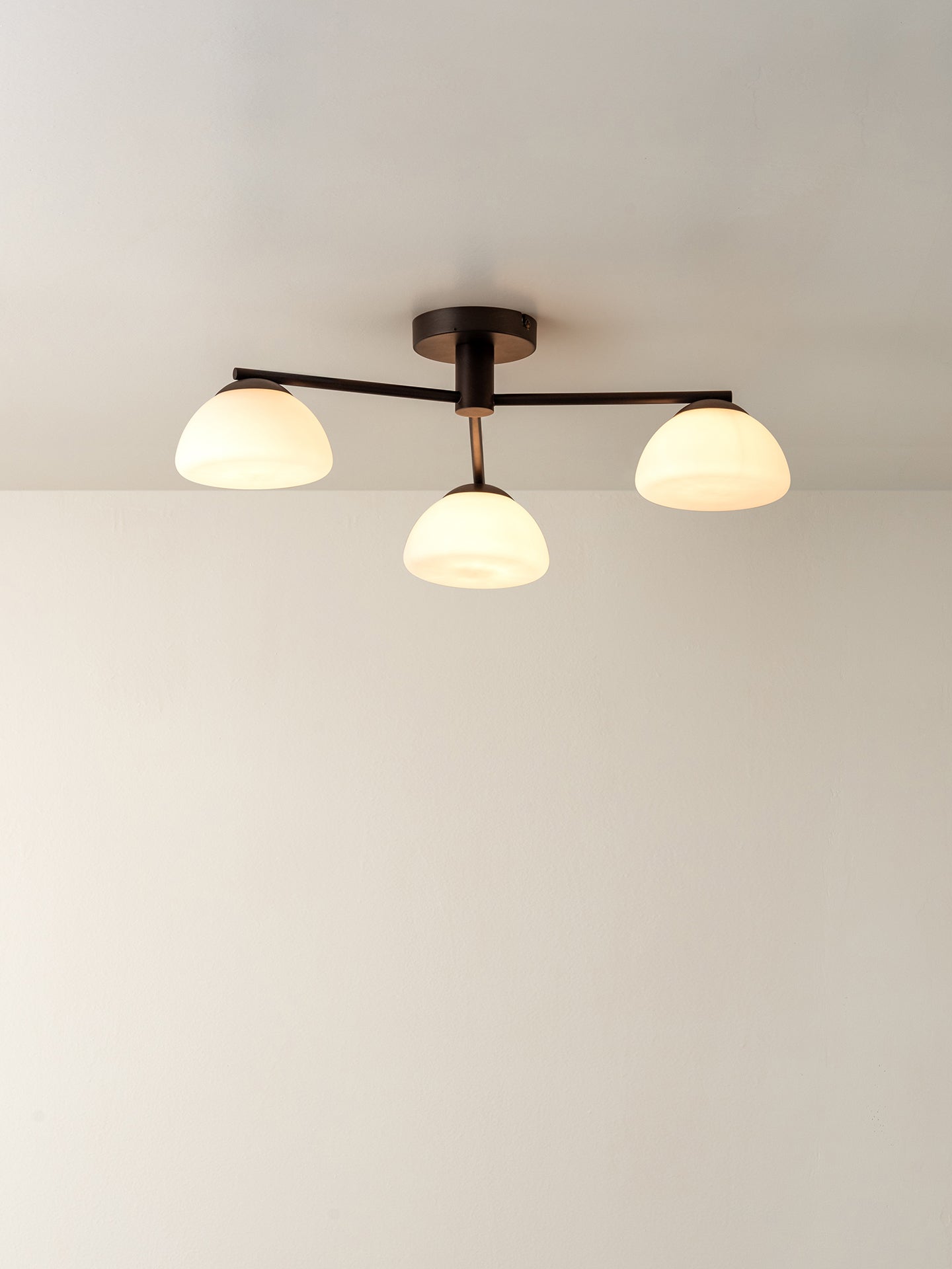 A modern three-light ceiling fixture with a matte black metal frame and frosted white glass shades, shown installed on a plain white ceiling.