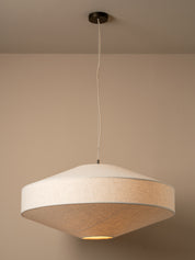 A modern pendant light with a wide, shallow conical shade made of textured beige fabric, suspended from a black ceiling canopy by a thin white cord against a warm beige wall.